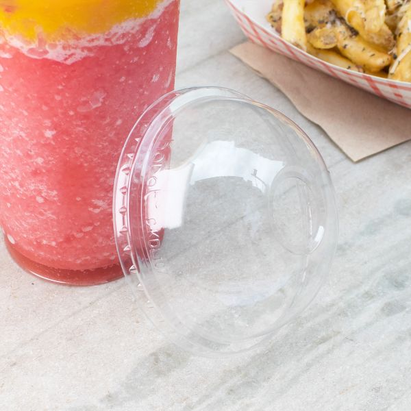 Clear Karat 107mm PET Plastic Dome Lid beside cup with smoothie