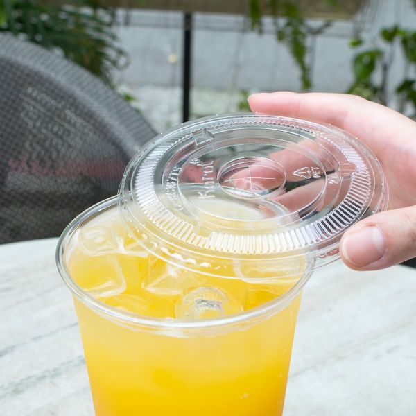 Clear Karat 107mm PET Plastic Flat Lids on cup with yellow drink