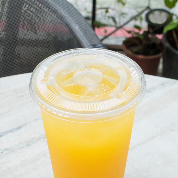 Clear Karat 107mm PET Plastic Flat Lids on cup with yellow drink