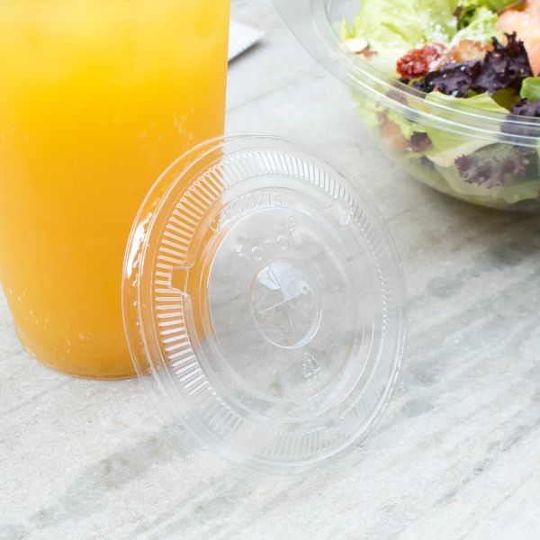 Clear Karat 107mm PET Plastic Flat Lids beside cup with yellow drink