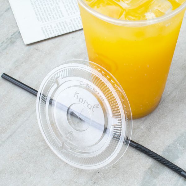 Clear Karat 107mm PET Plastic Flat Lids beside cup with yellow drink