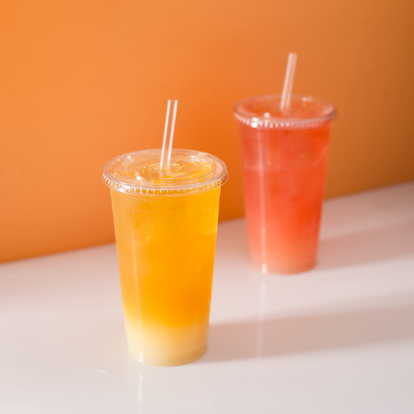 Clear Karat 32oz PET Plastic Cold Cups with one yellow and one orange drink with matching flat lids and straws