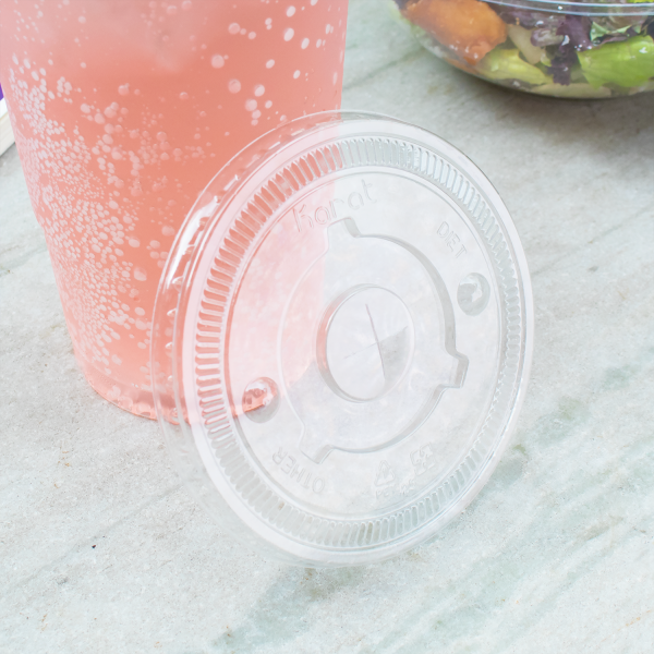Clear Karat 104.5mm PET Plastic Flat Lids beside pink drink