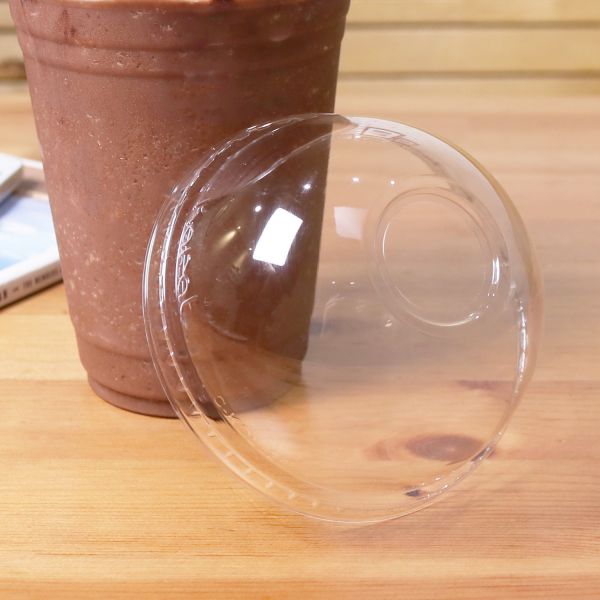 Clear Karat 98mm PET Plastic Dome Lids next to matching cup with chocolate frozen drink