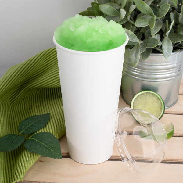 Clear Karat 90mm PET Plastic Dome Lids next to matching paper cup with green iced drink