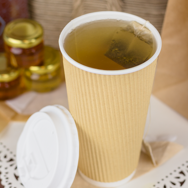Kraft Karat 20oz Ripple Paper Hot Cup filled with tea beside white dome sipper lid